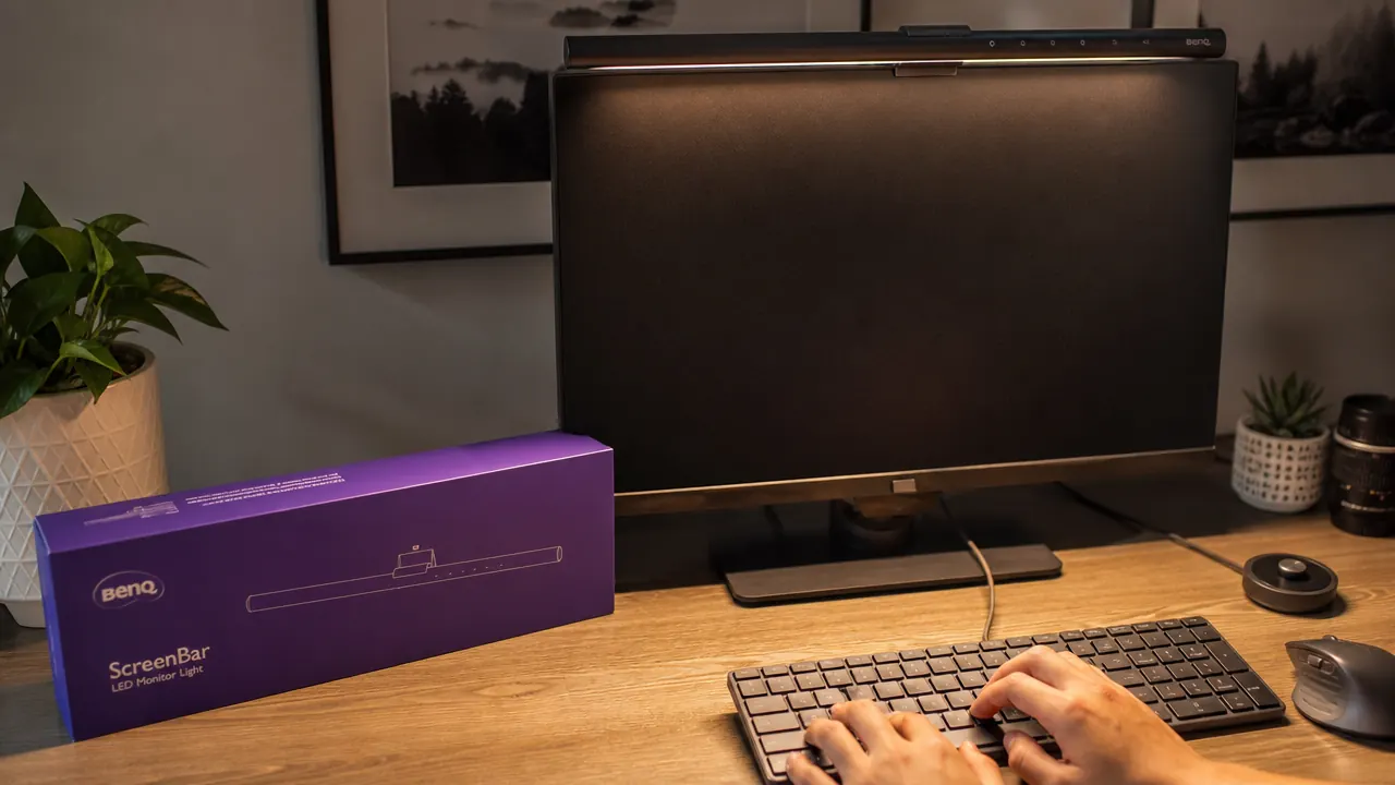 BenQ ScreenBar monitor light bar clipped to top edge of monitor, casting even warm light down onto a keyboard and desk