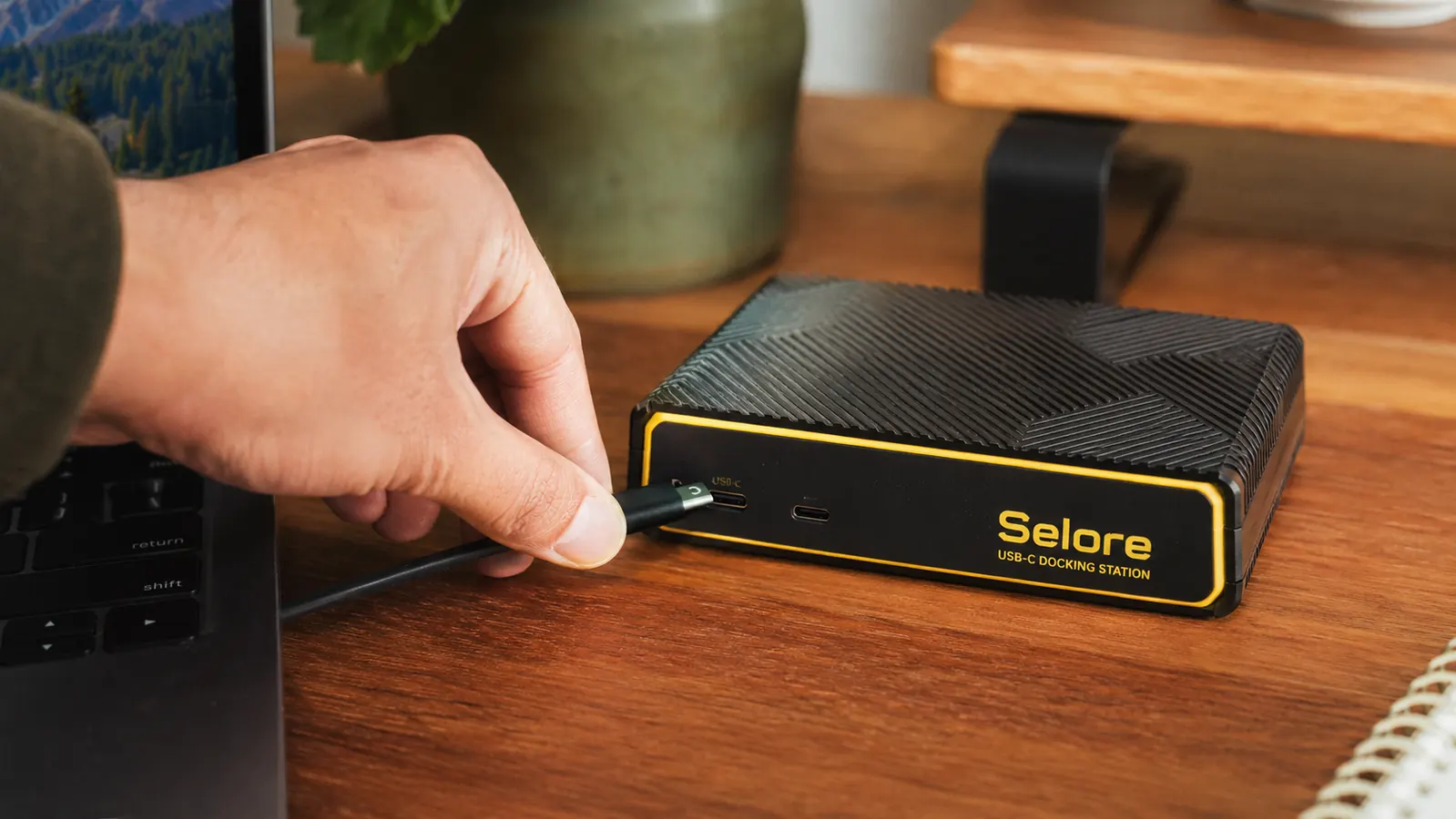 Hand placing a single USB-C cable into the Selore docking station sitting on a wood desk